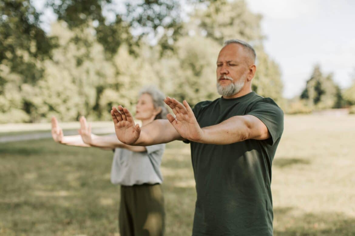 An elderly couple doing yoga with their arms outstretched